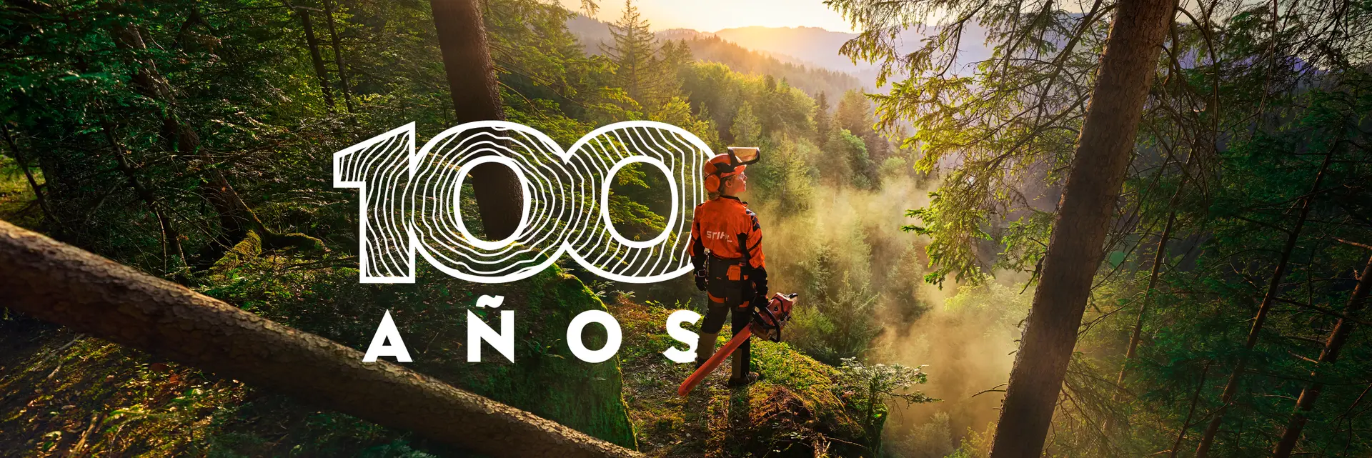 Bosque al amanecer con un operario de STIHL y su motosierra, junto al emblema de los 100 años de STIHL